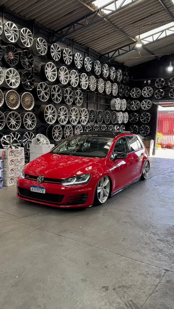 Golf GTI vermelho rebaixado dentro da loja da Fera, com a parede de rodas ao fundo.